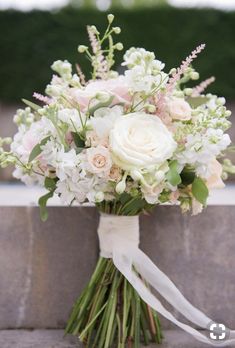 a bridal bouquet with white and pink flowers on the side of a stone wall