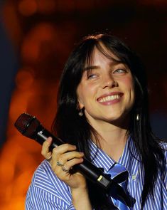 a woman holding a microphone in her right hand and smiling at the camera while wearing a blue striped shirt