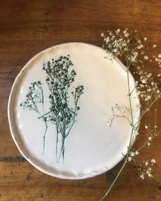 a plate with some flowers on it sitting on top of a wooden table next to a plant