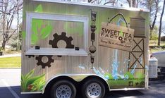 a food truck parked in a parking lot with trees and grass on the side of it