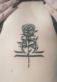 a woman's back with a rose and cross tattoo on her left side ribcage