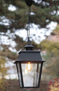 an outdoor light hanging from the side of a building with trees in the back ground