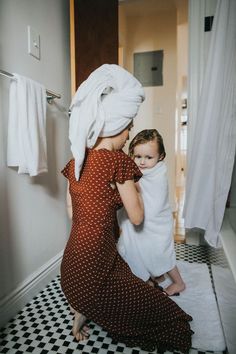 a woman holding a baby wrapped in a towel while standing next to a bathroom sink