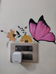 a pink butterfly sitting on top of a wall next to a white outlet with two black outlets