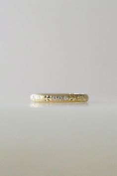 a yellow gold wedding band with three diamonds on it, sitting on a white surface