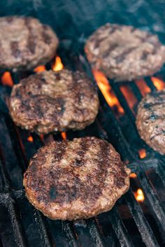 hamburgers cooking on the grill with flames coming out of it's center piece