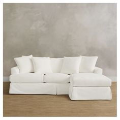 a white sectional couch with pillows on the top and bottom part, in front of a gray wall