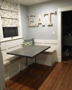 a table and bench in a room with wood flooring next to a wall that says eat