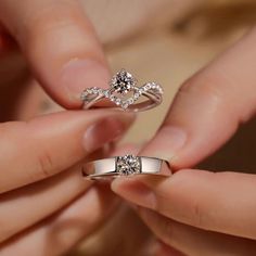 two hands holding an engagement ring and another hand with wedding rings on it, both showing their fingers