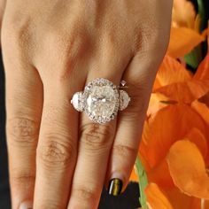 a woman's hand with an engagement ring on top of her finger and orange flowers in the background