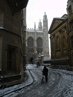 a person riding a bike down a snow covered street in front of a tall building