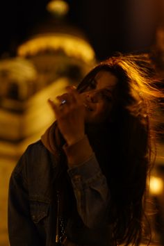 a woman standing in front of a building with her hair blowing in the wind while talking on a cell phone