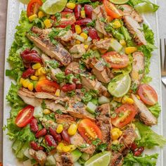 a white platter filled with chicken, tomatoes, corn and lettuce salad