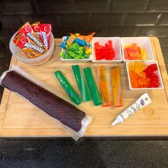 some gummy bears are sitting on a cutting board next to other candy bars and candies