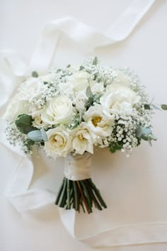 a bridal bouquet with white roses and baby's breath on a white cloth