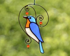 a blue and orange bird hanging from a metal wire with red beads on it's tail