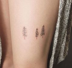 three pine trees tattoo on the right side of the thigh and behind the leg are small black contours