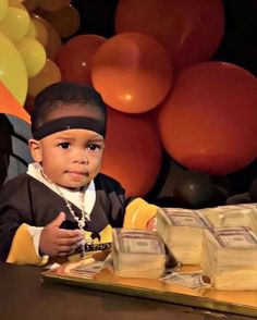 a young boy sitting at a table in front of some bags of money and balloons