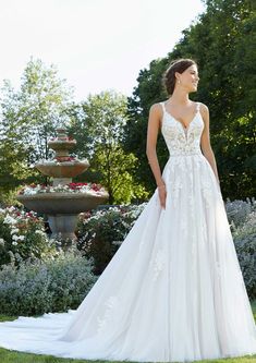 a woman in a white wedding dress standing on the grass near some bushes and flowers