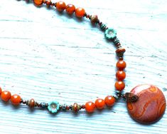 18"   Agate necklace made w/rustic red orange Jasper gemstone pendant,  8 mm Carnelian colored Agate beads, 4 mm Carnelian colored agate beads, 12 mm aqua & rustic red Lampwork accent beads, 8 mm accent Picasso glass beads, patina turquoise Bali style accent beads, 10 mm green Picasso flower glass accent beads, 6 mm caramel Picasso beads w/aqua finish, 3 mm patina turquoise disc spacers, 3 mm Picasso glass beads, antique brass bead caps, brass spacer beads and brass lobster claw clasp. Red Jasper Necklace, Bali Fashion, Jasper Necklace, Agate Necklace, Red Jasper, Jasper Gemstone, Aqua Green, Stunning Necklace, Agate Beads