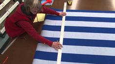 an older woman is measuring the length of a blue and white striped rug on a table