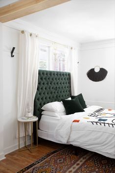 a bed with white sheets and green headboard in a bedroom next to a window