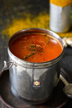 a metal pot filled with red soup on top of a wooden table next to spoons