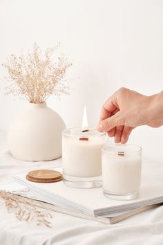 a person lighting a candle on top of a book next to a vase with flowers