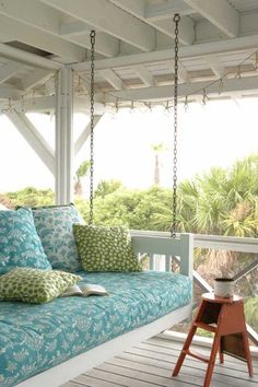 a porch swing bed with blue and green pillows on the back, hanging from a pergolated roof