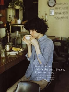 a woman sitting at a table drinking from a cup