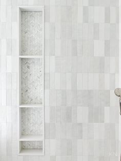 a white tiled bathroom with a shelf above the tub and shower head in the corner