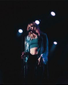 a woman standing in front of a microphone on top of a stage with lights behind her