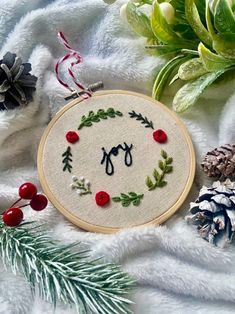 an embroidered christmas ornament surrounded by pine cones, berries and evergreen needles on a white blanket