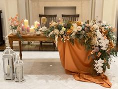 an arrangement of flowers and candles on the floor in front of a table with chairs