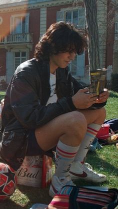 a young man sitting on the grass looking at his cell phone while holding a soccer ball