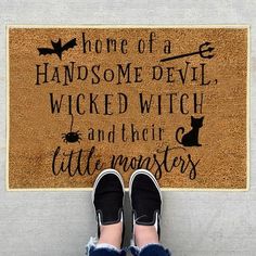 someone is standing in front of a door mat that says home of a handsome devil, witch and their little monsters