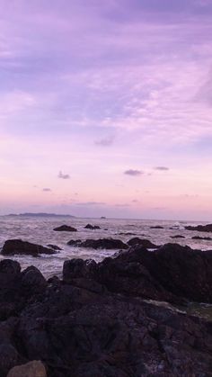 a person standing on rocks near the ocean at sunset with an umbrella over their head