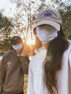 two people wearing face masks and standing in the grass with trees behind them at sunset