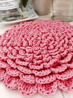 a pink crocheted dishcloth sitting on top of a counter next to a cup