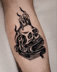 a black and white tattoo on the arm of a man with a skull reading a book