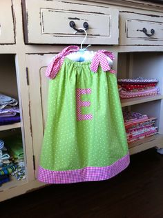 a green and pink dress hanging on a clothes rack in front of an old dresser