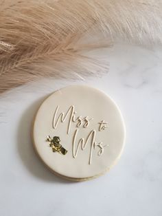 a cookie with the words mrs to mrs written on it next to some brown feathers