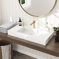 a white sink sitting under a round mirror next to a wooden table with towels on it