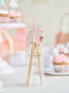 two wooden sticks in a clear box with pink frosted cupcakes behind them