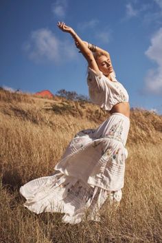 a woman in a white dress is standing in the grass and stretching her arms up