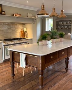 a large white kitchen island in the middle of a wood floored room with hanging lights