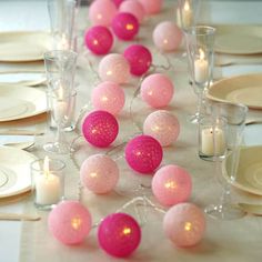 the table is set with pink and white balls, candles, and plates on it