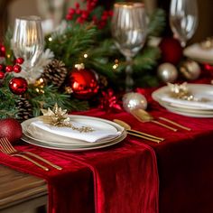 the table is set for christmas dinner with red and gold decorations, silverware, and candlesticks