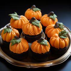 cupcakes decorated with orange frosting and green leaves are on a silver plate