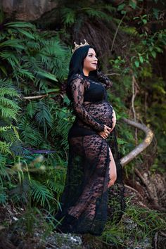 a pregnant woman wearing a black lace gown and crown standing in the woods with her hands on her stomach